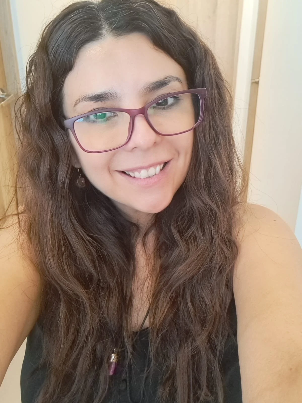 Mujer sonriendo con lentes de marco morado y cabello rizado largo